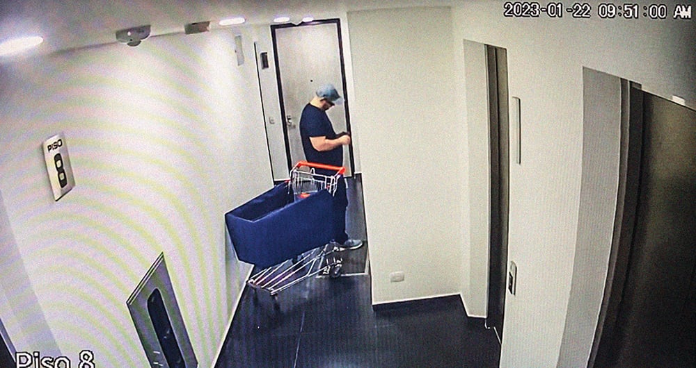 DOMINGO 22 DE ENERO, 9:50 A. M. John Poulos llega al apartamento con un carrito de mercado que obtiene en alguno de los pisos del edificio. Ingresa al apartamento y cierra la puerta.