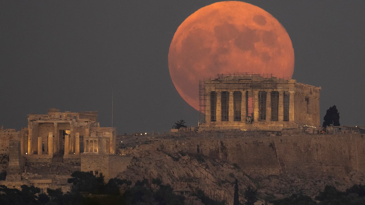 La Luna Llena se eleva detrás de la colina de la Acrópolis y el antiguo Templo del Partenón, en Atenas, Grecia.