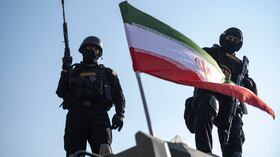 Dos miembros armados de las fuerzas especiales de la policía iraní posan detrás de una bandera iraní colocada en un vehículo militar blindado