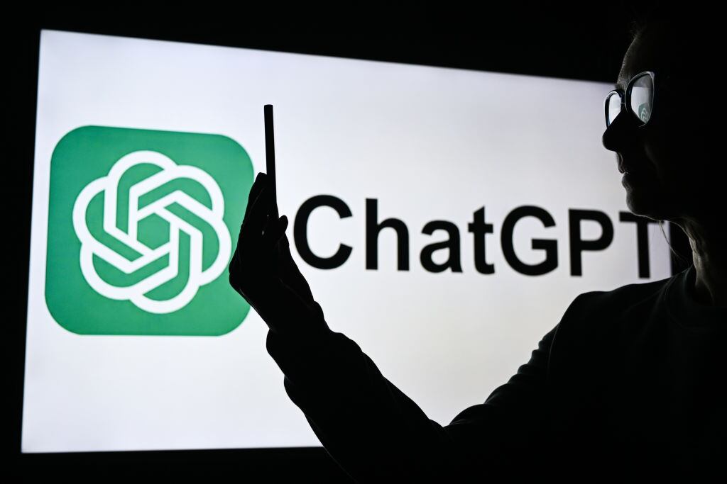 Una mujer sostiene un teléfono celular frente a una pantalla de computadora que muestra el logotipo de ChatGPT, el 10 de febrero de 2025, en Edmonton, Canadá. (Foto de Artur Widak/NurPhoto vía Getty Images)
