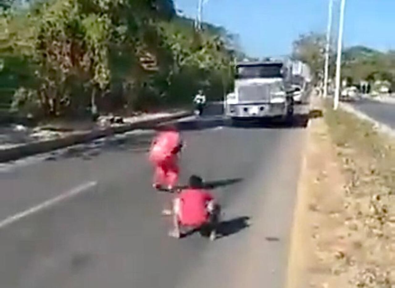 Los dos niños visten de rojo, se bajan a la carretera, bailan y saltan y luego corren hacia el costado
