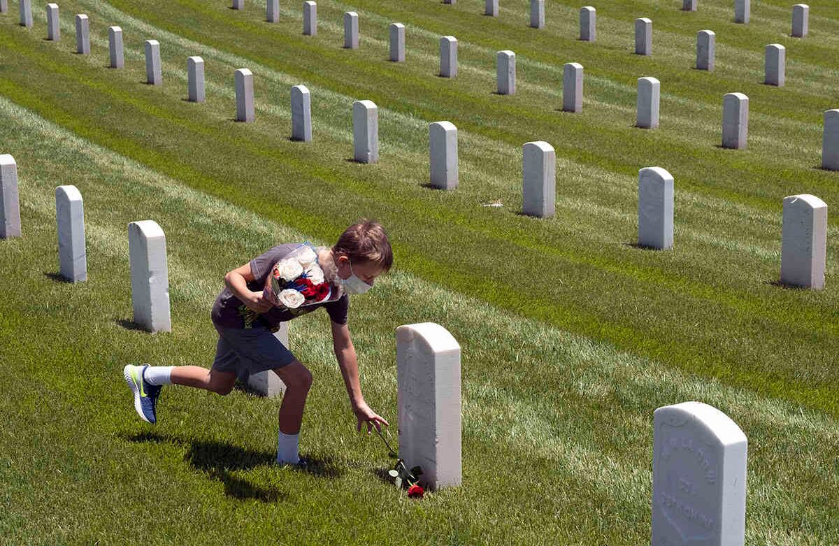 Un niño con una tapabocas protector para el coronavirus coloca una flor al pie de la tumba de un soldado caído en el Cementerio Nacional de Los Ángeles para honrar a los soldados caídos y a los trabajadores de la salud en Los Ángeles, el Día de los Caídos el lunes 25 de mayo de 2020. La conmemoración del Día de los Caídos en el cementerio se llevó a cabo sin la asistencia del público debido al brote de coronavirus. (Foto AP / Richard Vogel)