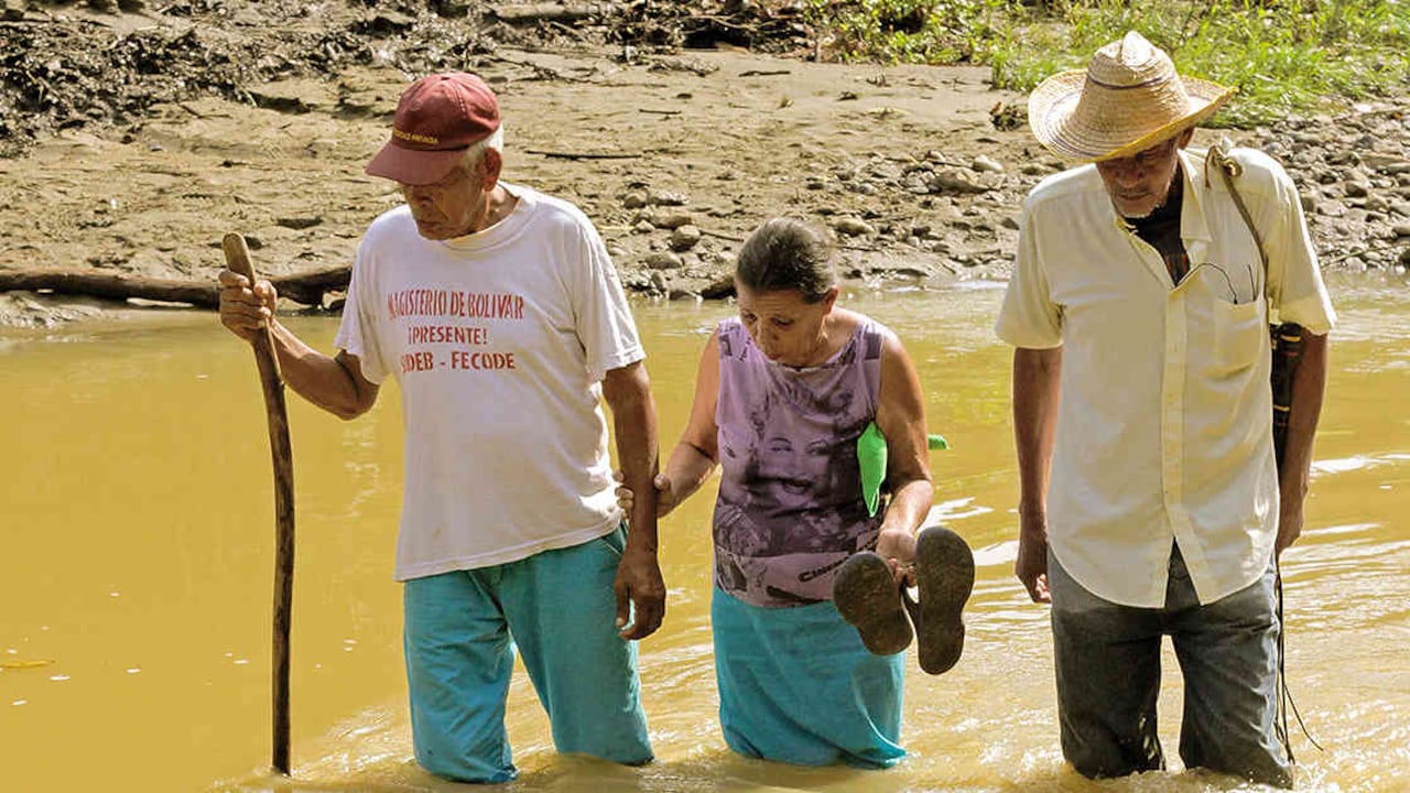 Julio Acevedo, Madis Díaz y Francisco Acevedo deben cruzar el arroyo crecido que dejó el invierno para poder trabajar la parcela restituída.