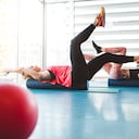 Dos jóvenes atletas de fitness haciendo un ejercicio de dead bug en un rodillo de espuma, para trabajar en sus músculos centrales y estabilidad.