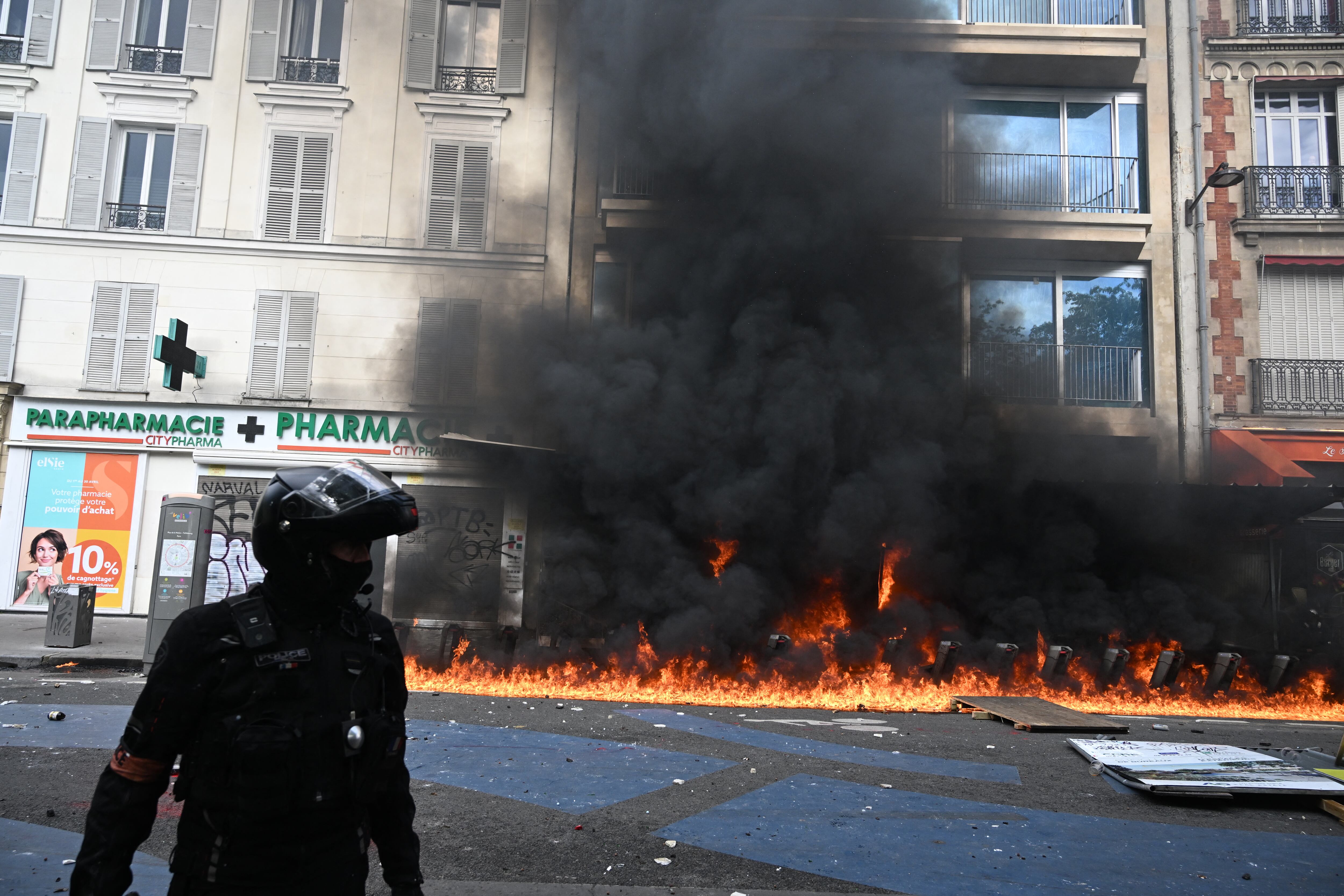 Un oficial de policía francés de la brigada motorizada de represión de la acción violenta (Brav-M o Brigade de repression de l'actionviolence motorisee) se encuentra frente a un incendio durante una manifestación el Primero de Mayo (Día del Trabajo) para conmemorar el día internacional de la trabajadores, más de un mes después de que el gobierno impulsara una impopular ley de reforma de las pensiones en el parlamento, en París, el 1 de mayo de 2023. - Los partidos de oposición y los sindicatos han instado a los manifestantes a mantener su campaña de tres meses contra la ley que aumentará el edad de jubilación de 62 a 64. (Foto de Alain JOCARD / AFP)