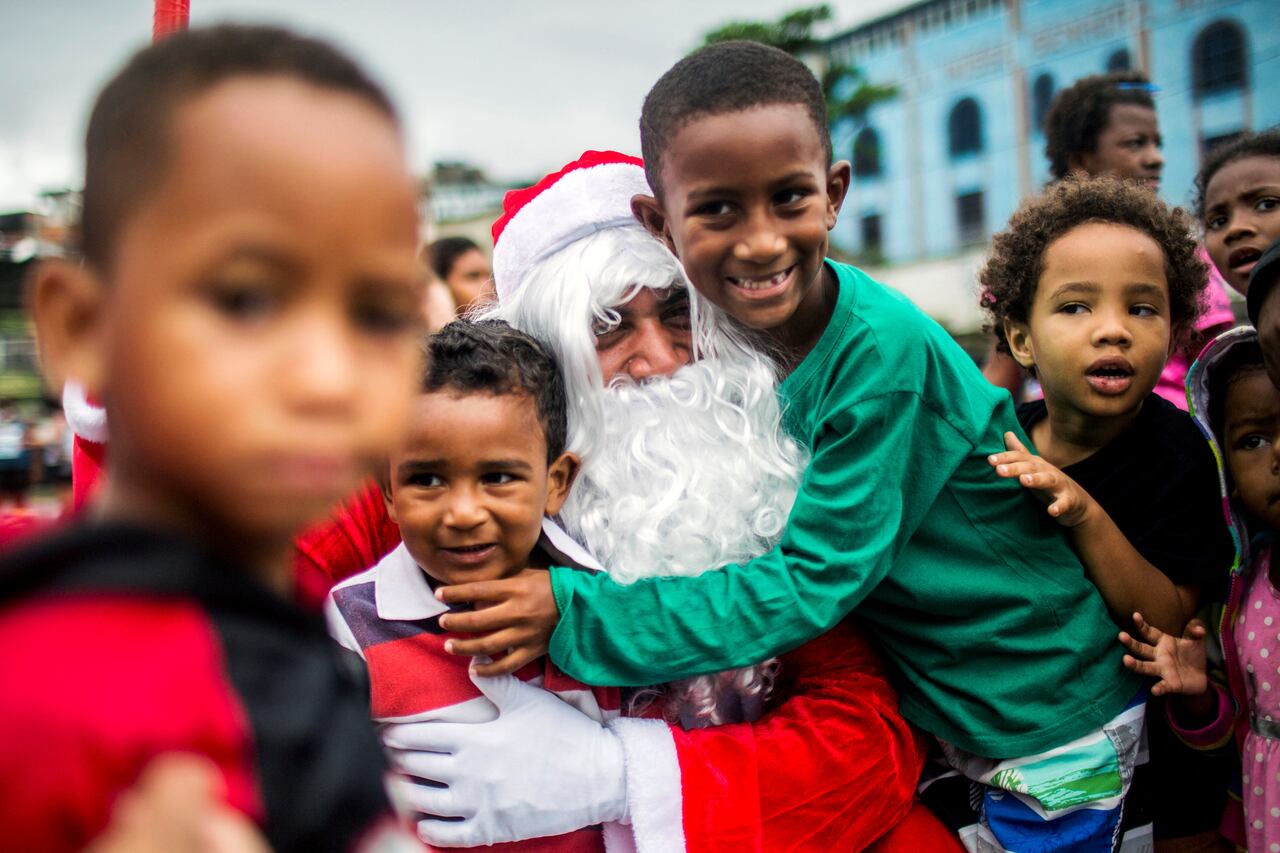 Un hombre disfrazado de Papá Noel abraza a niños durante una distribución de comida navideña organizada por la ONG Central nica das Favelas (CUFA) en el barrio de chabolas del Complejo Penha, comúnmente conocido como Complejo Alemao, en Río de Janeiro, Brasil, el 23 de diciembre de 2021