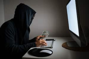 Foto de un hombre adulto para ocultar su identidad y usar la computadora para piratear. El fondo es oscuro y la atmósfera es futurista. El esta usando un teclado