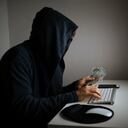 Foto de un hombre adulto para ocultar su identidad y usar la computadora para piratear. El fondo es oscuro y la atmósfera es futurista. El esta usando un teclado