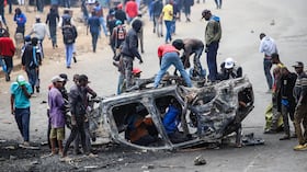 Personas retiran piezas de un vehículo incendiado durante una huelga de transporte público por el aumento de los precios del combustible en Nairobi, Kenia, el lunes 18 de mayo de 2026.