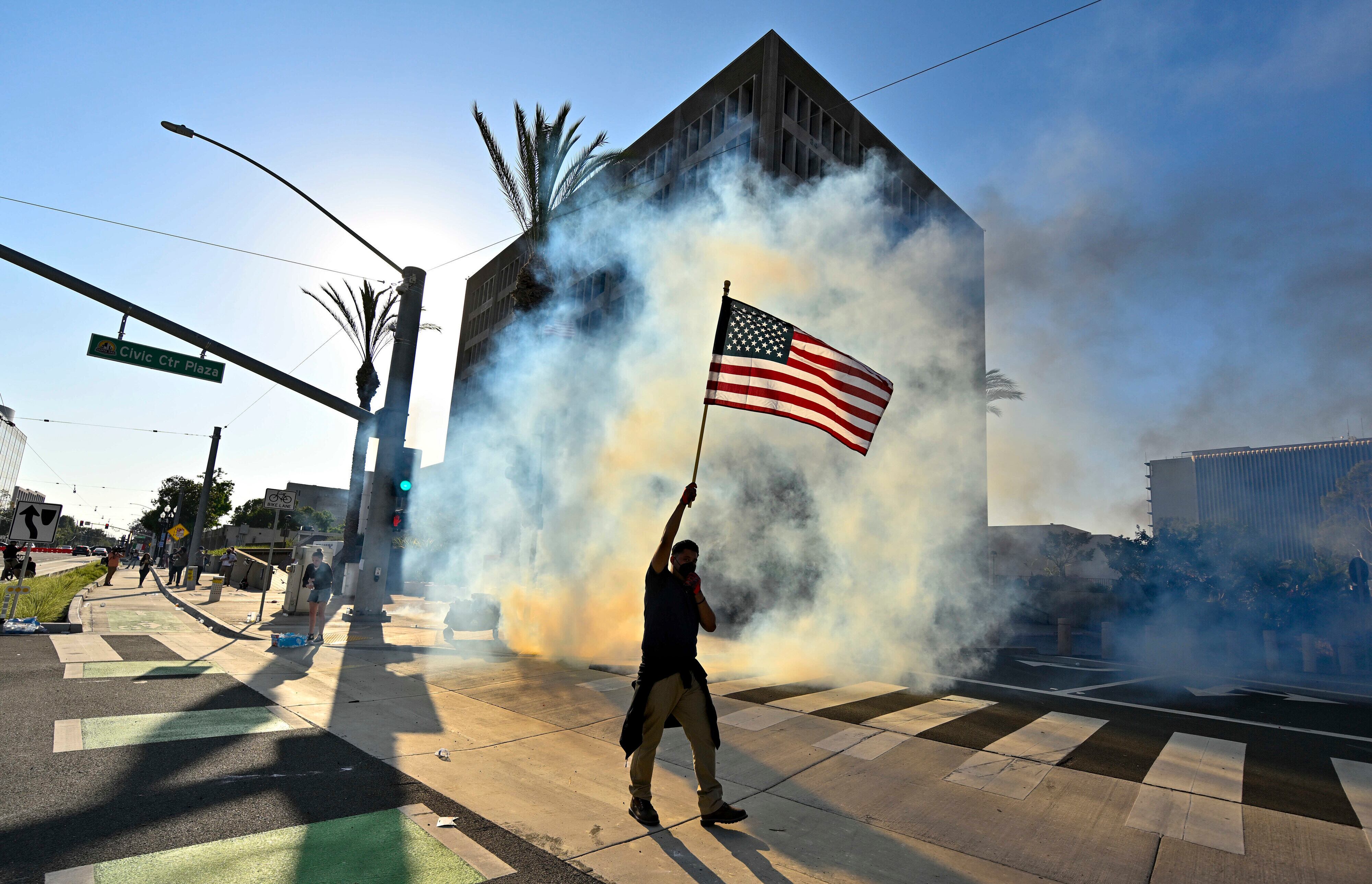 Un manifestante iza la bandera estadounidense después de que la policía usara gases lacrimógenos y granadas aturdidoras en el Edificio Federal de Santa Ana, California.