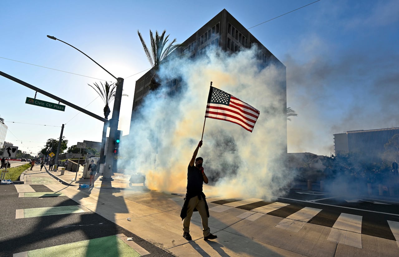 Un manifestante iza la bandera estadounidense después de que la policía usara gases lacrimógenos y granadas aturdidoras en el Edificio Federal de Santa Ana, California.