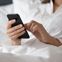 La mujer se despertó acostada en la cama debajo de la manta, use el teléfono para aprender una nueva aplicación, planifique el día, verifique la lista de tareas diarias del calendario personal, busque información, revise los mensajes del buzón de correo electrónico, comience el día con el concepto de gadget