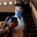 Empresario mediante teléfono móvil en el aeropuerto con máscara protectora