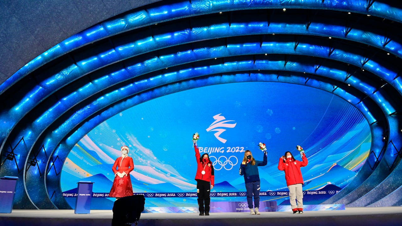 An hostess stands next to Silver medallist Spain's Queralt Castellet (L), gold medallist USA's Chloe Kim (C) and bronze medallist Japan's Sena Tomita (R) during the snowboard women's halfpipe victory ceremony of the Beijing 2022 Winter Olympic Games at the Zhangjiakou Medals Plaza in Zhangjiakou on February 10, 2022. (Photo by Tobias SCHWARZ / AFP)