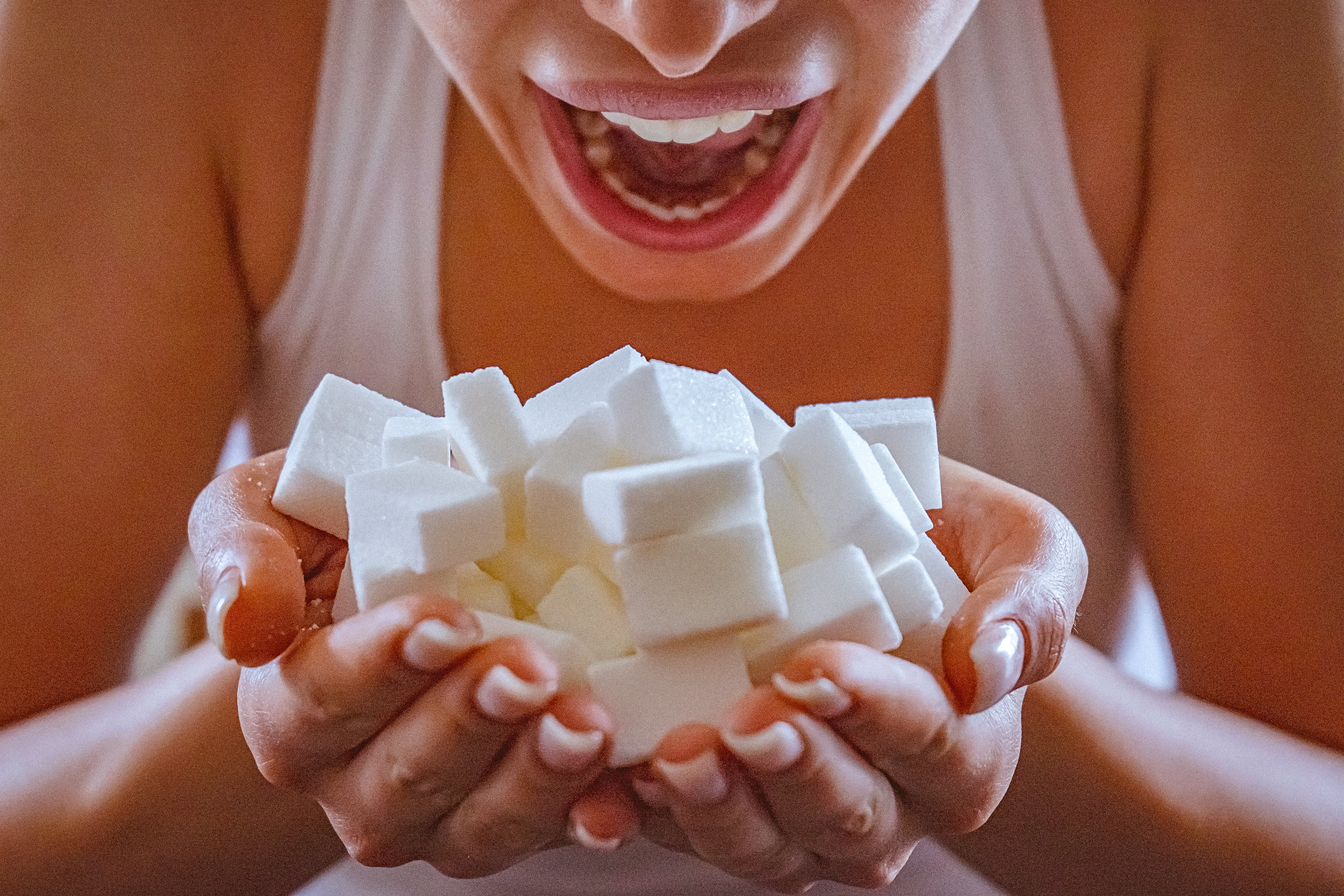 Close-up of woman holding a hands full of sugar cubes in front of her open mouth