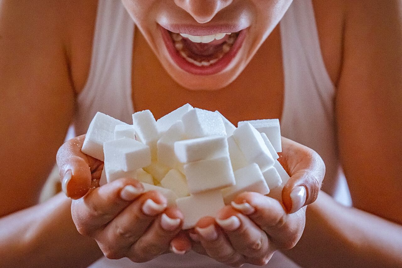 Close-up of woman holding a hands full of sugar cubes in front of her open mouth