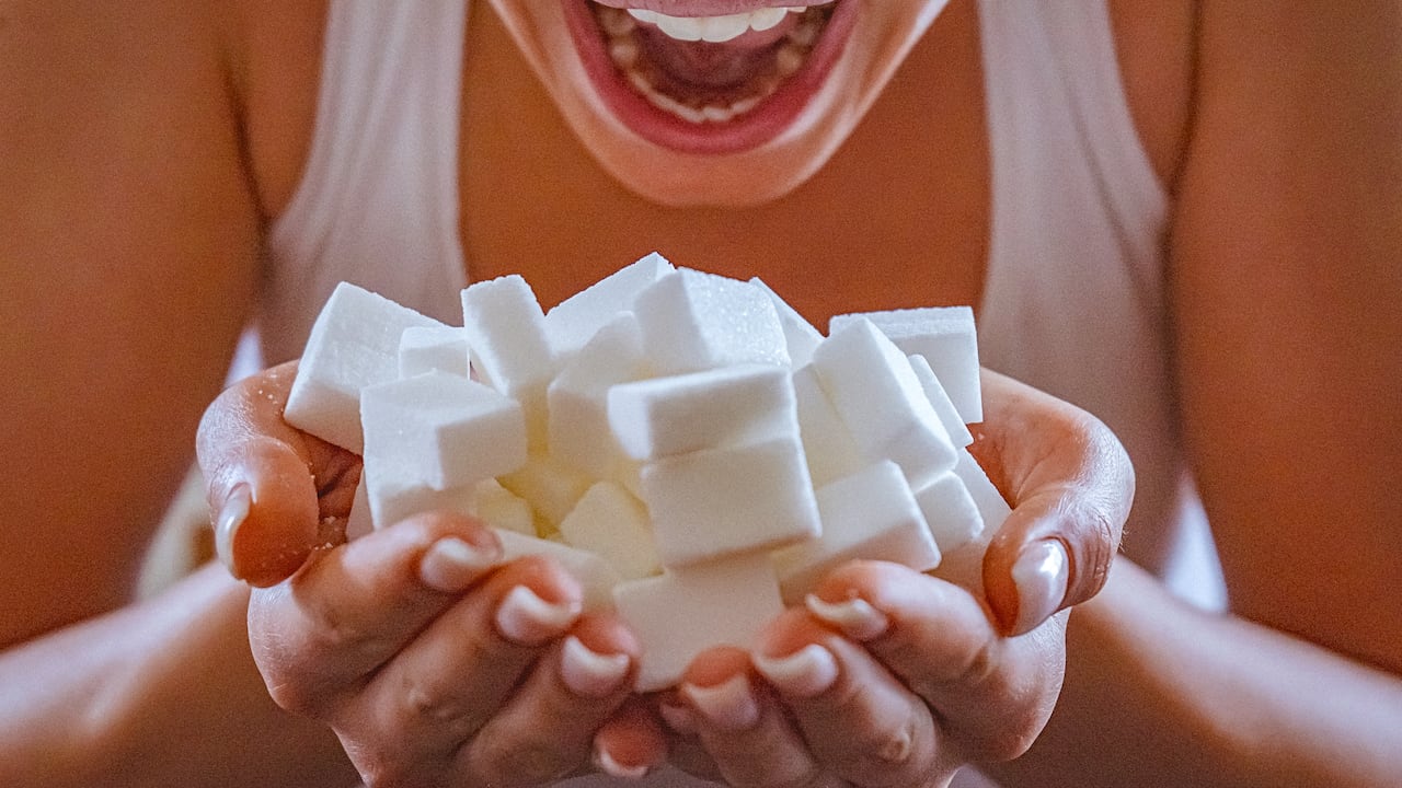 Close-up of woman holding a hands full of sugar cubes in front of her open mouth