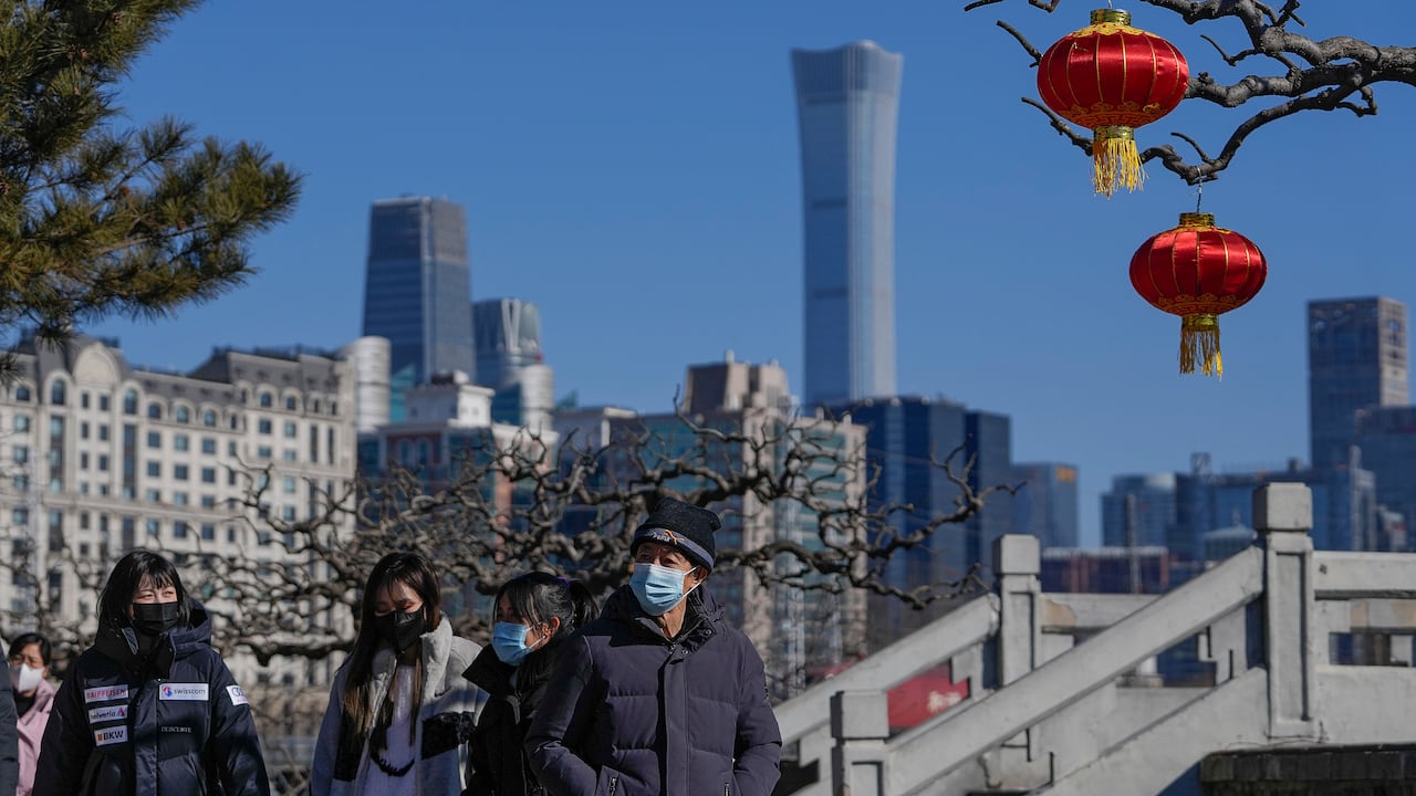 People wearing face masks to help protect from the coronavirus walk by lantern decorations for the upcoming Lunar New Year in a park seen against the city skyline in Beijing, Thursday, Jan. 27, 2022. (AP Photo/Andy Wong)
