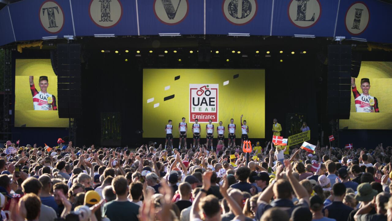 2020 and 2021 Tour de France winner Tadej Pogacar of Slovenia, far right, and on screen left and right, lines up with UAE Team Emirates riders during the team presentation ahead of the Tour de France cycling race in Copenhagen, Denmark, Wednesday, June 29, 2022. The race starts Friday, July 1, the first stage is an individual time trial over 13.2 kilometers (8.2 miles) with start and finish in Copenhagen. (AP/Daniel Cole)