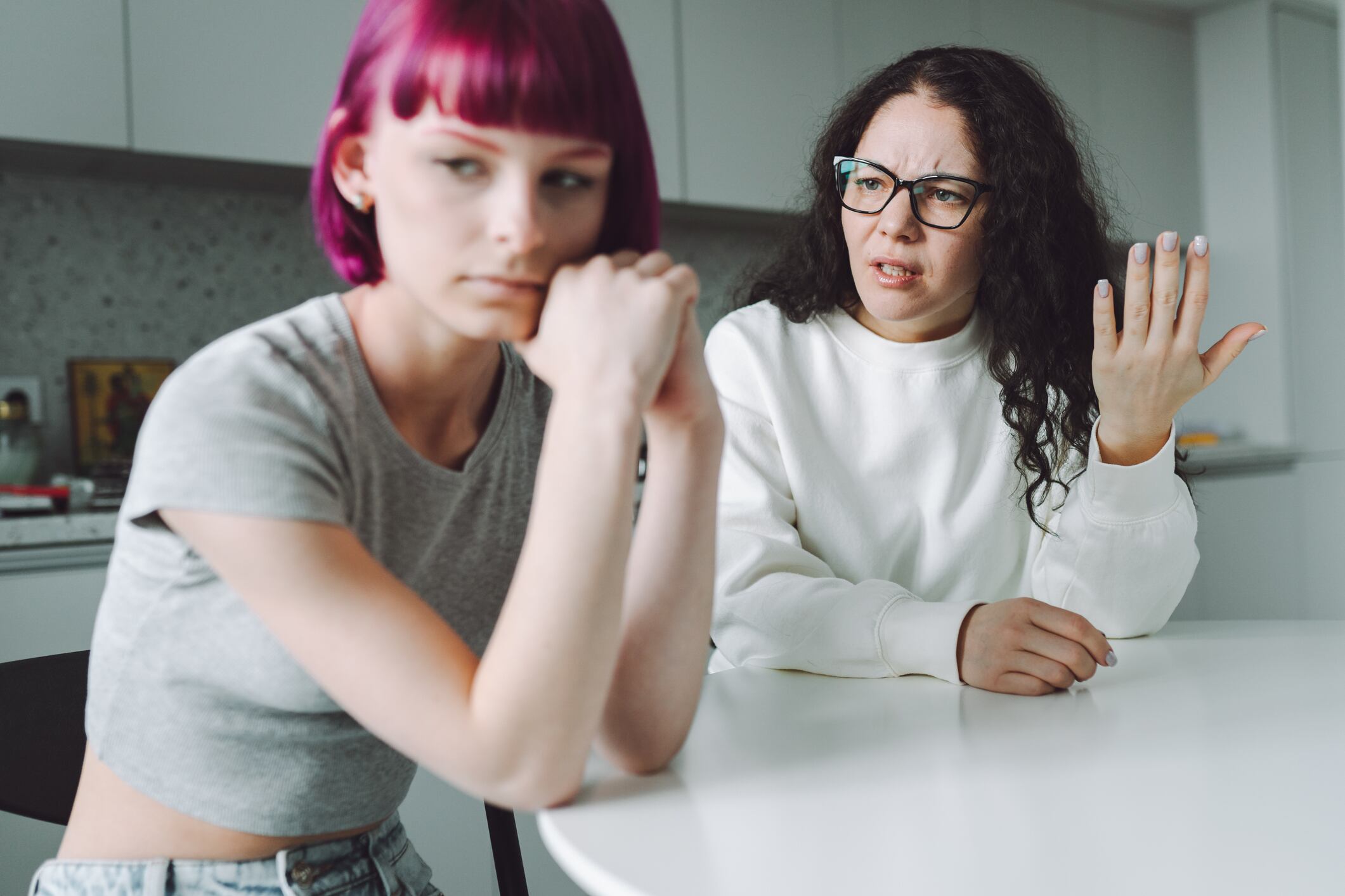 Pink bobbed haired teen girl keeping silence, having a conflict with her mother, sitting in the kitchen