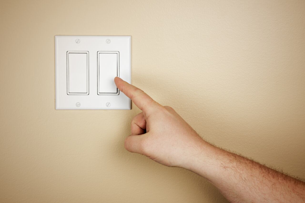 Una mano masculina se mueve para apagar un interruptor de luz.