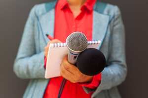 Female reporter at press conference, writing notes, holding microphone