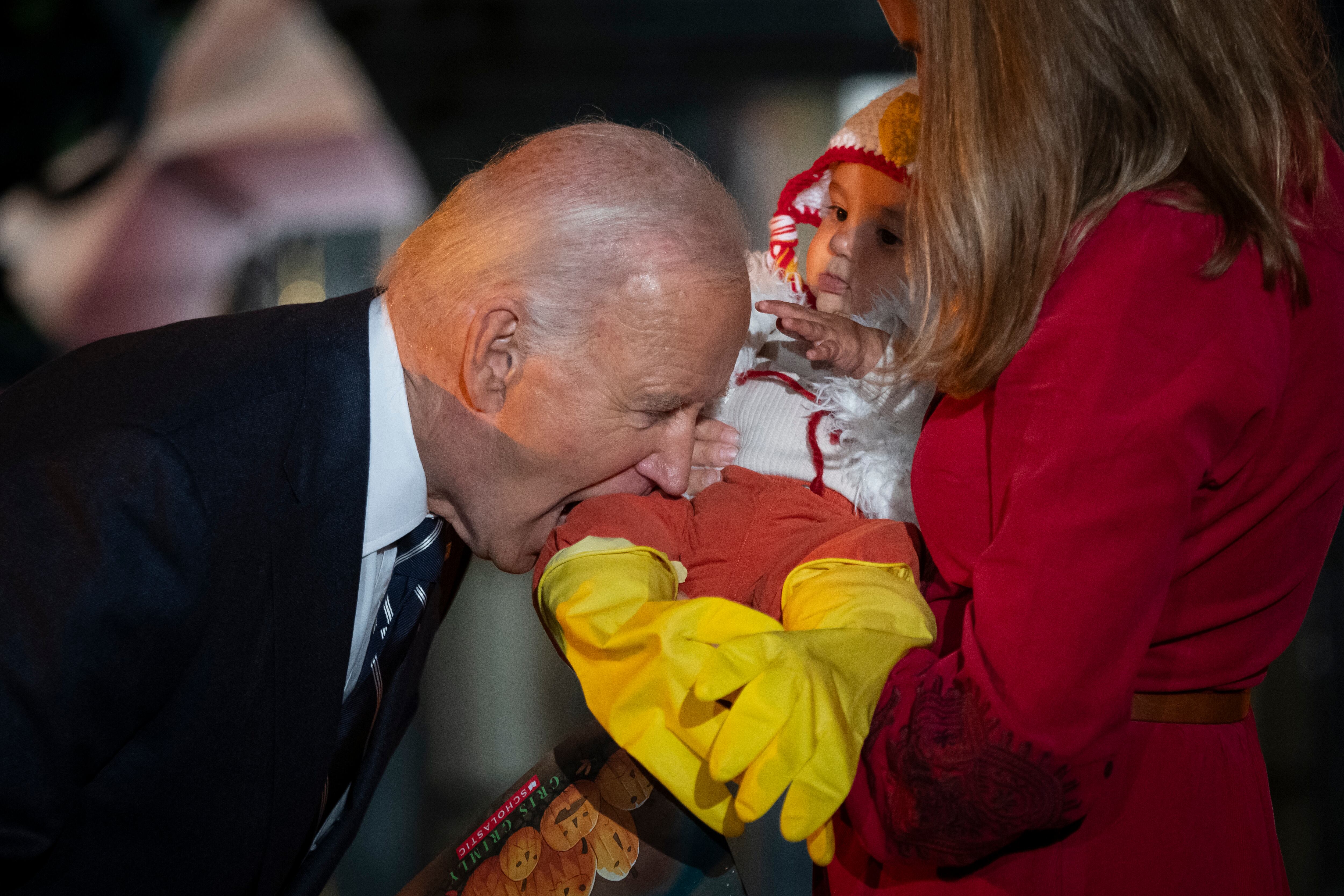 El presidente Joe Biden, en broma, muerde la pierna de un bebé, mientras él y la primera dama Jill Biden reciben a estudiantes del área local, niños relacionados con el ejército y familias del vecindario para pedir dulces, antes de Halloween el jueves, en el jardín sur del Casa Blanca en Washington el miércoles 30 de octubre de 2024. (Foto AP/Ben Curtis)