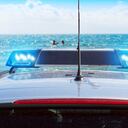police car with blue flashing lights on the beach against blue sea and sky