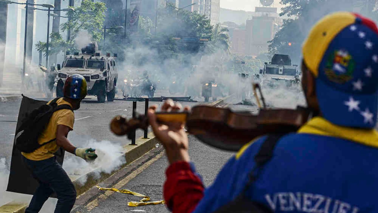 Interpretando con un violín el himno de Venezuela y el tradicional joropo Alma Llanera, Wuilly Arteaga avanzó el 8 de mayo hacia los cuerpos de seguridad bajo una lluvia de bombas lacrimógenas. Fue su homenaje a un músico de 17 años muerto días antes en una manifestación. Foto: AFP.