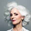 Mature woman with medium length, big, wavy, silvery, grey hair in front of grey background wearing make up red lip stick, portrait.