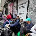 Migrants sit in a queue outside of The Roosevelt Hotel that is being used by the city as temporary housing, Monday, July 31, 2023, in New York. (AP Photo/John Minchillo)
