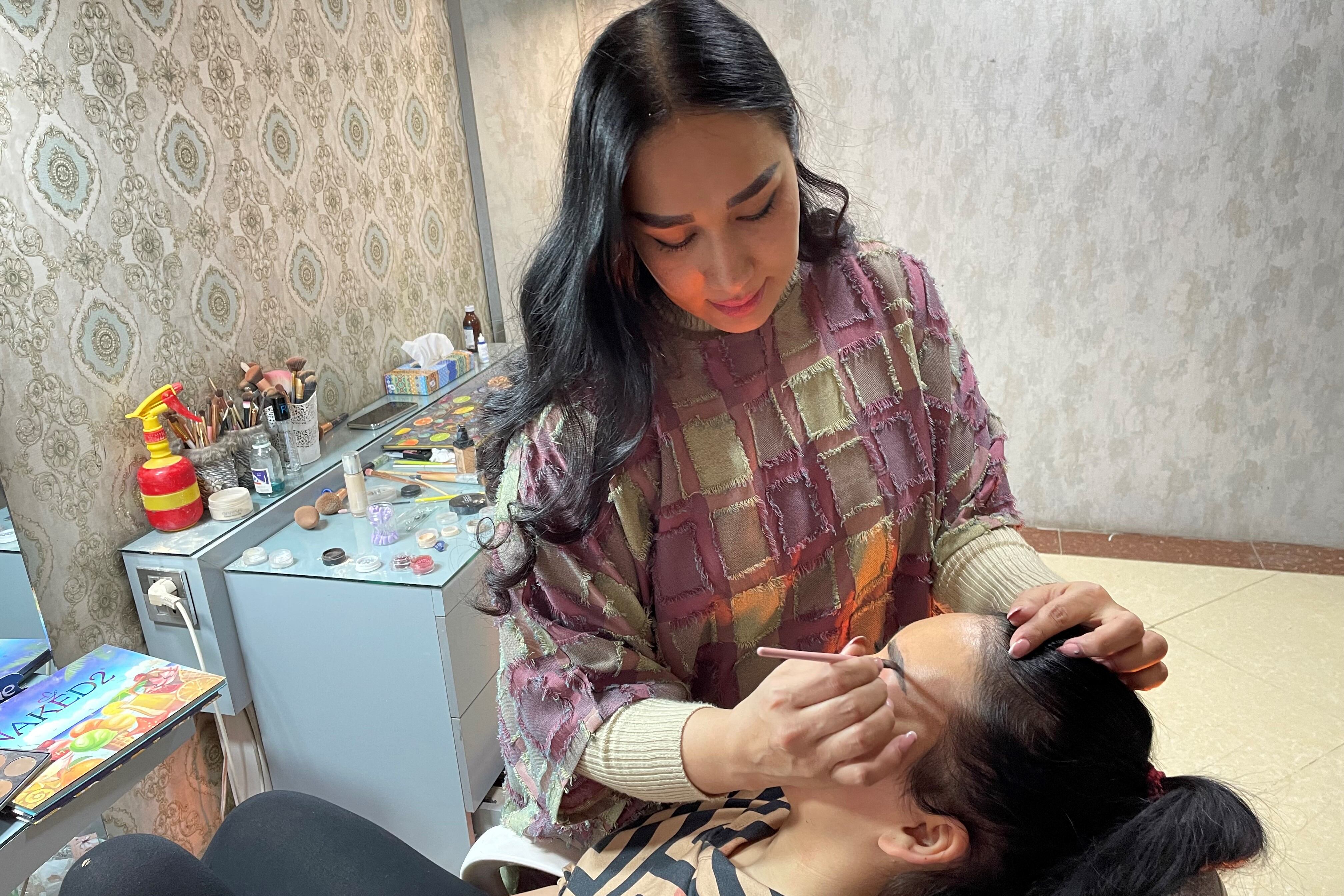 In this photograph taken on October 18, 2021, a beautician applies make-up to a customer at a beauty salon in Kabul. - It is one of the last places in Kabul where women can meet outside their households, a bubble of freedom and even frivolity away from the gaze of men. (Photo by Maryke Vermaak / AFP) / TO GO WITH Afghanistan-women-beauty,SCENE by Daphne Rousseau