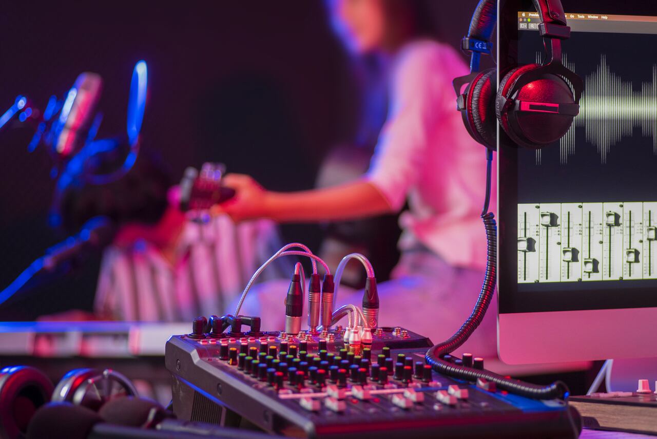 Close up instruments ,musician is background. Headphones hang on microphone with sound mixer board in home recording studio.