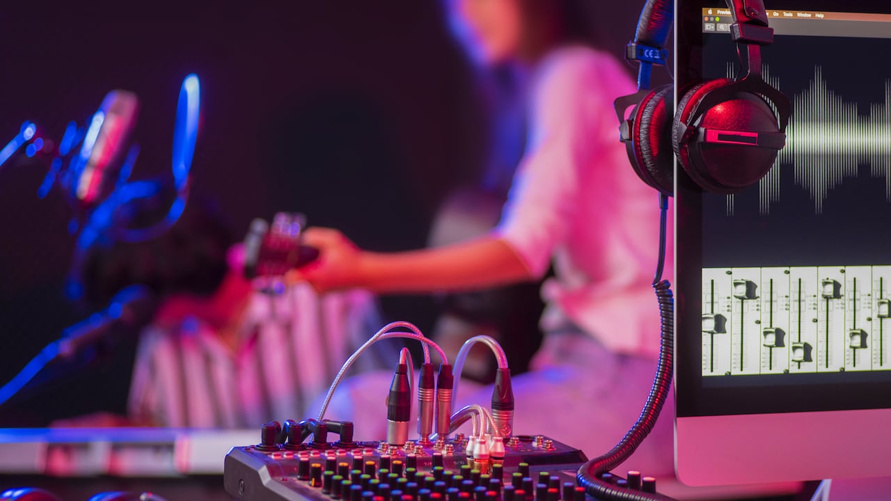 Close up instruments ,musician is background. Headphones hang on microphone with sound mixer board in home recording studio.