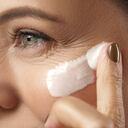 Beautiful middle aged woman applying anti-aging cream on her face on gray