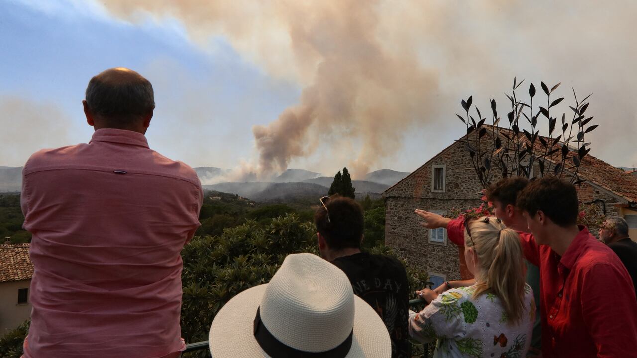 La gente en el pueblo de Grimaud, en el departamento de Var, observa cómo los incendios forestales se desatan en el sureste de Francia el 17 de agosto de 2021. (Photo by Valery HACHE / AFP)