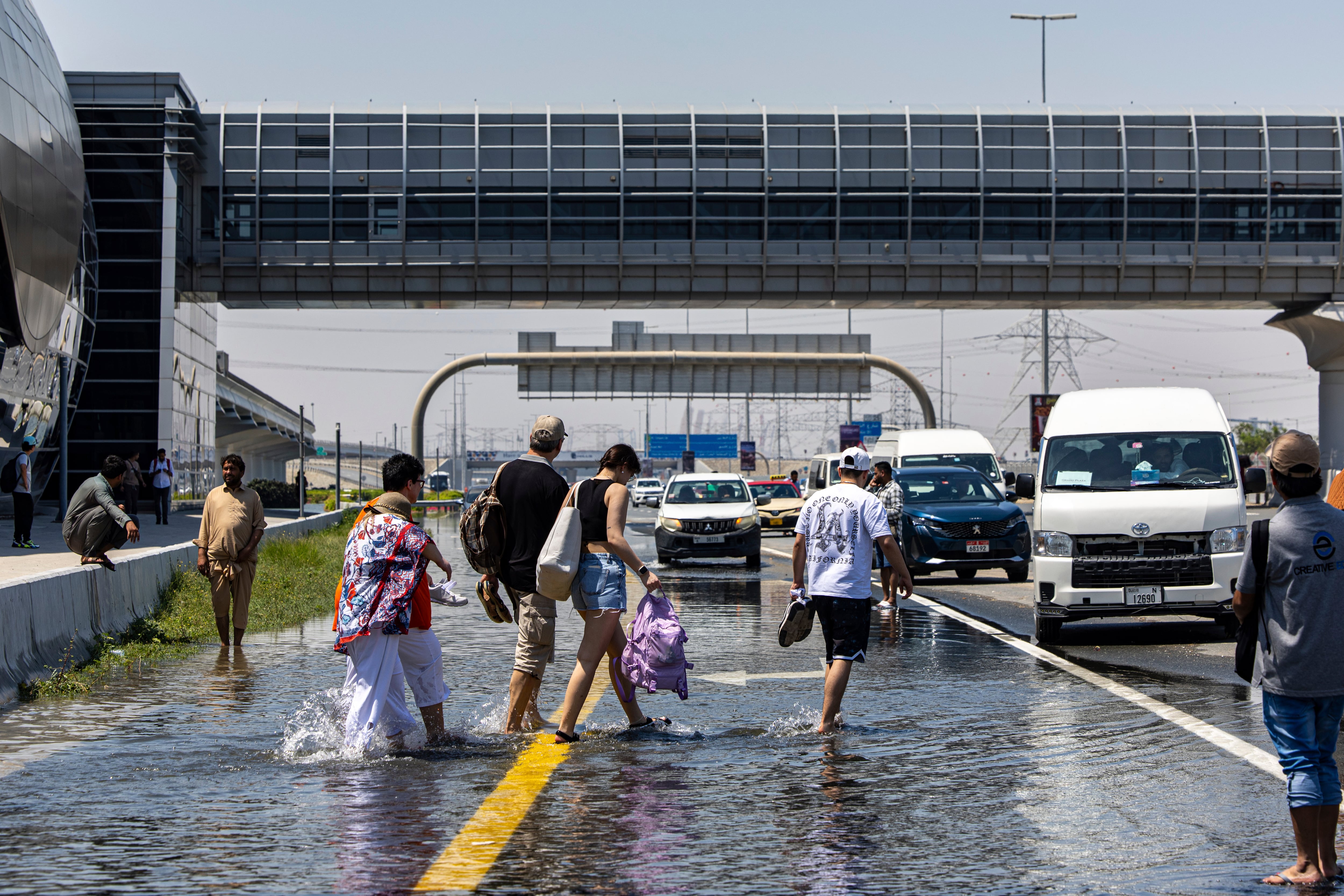 La gente camina entre las inundaciones causadas por las fuertes lluvias mientras esperan el transporte en la autopista Sheikh Zayed Road en Dubai, Emiratos Árabes Unidos, el jueves 18 de abril de 2024.