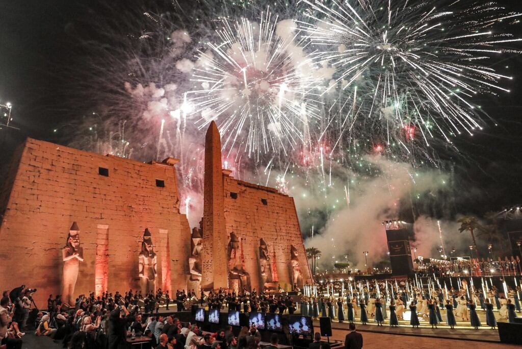Los fuegos artificiales iluminan el cielo durante la ceremonia oficial de inauguración de la "Rams Road"  en la entrada del Templo de Luxor (construido alrededor del 1400 a. C.) en la ciudad del mismo nombre en el sur de Egipto, el 25 de noviembre. 2021. El obelisco gemelo del templo de Luxor se encuentra actualmente en la Place de la Concorde de París. - Egipto inauguró el 25 de noviembre en una grandiosa ceremonia nocturna el "Camino de los Rams" (Tareeq al-Kebbash en árabe), un camino pavimentado de arenisca de 2700 metros de largo bordeado de estatuas con cabezas de carnero y esfinges que datan de más de 3000 años, conectando el Templo de Luxor con el Templo de Karnak. Llamado "El Camino de Dios" en la mitología del Antiguo Egipto, sus estatuas de carnero, una encarnación de la antigua deidad egipcia Amón, fueron enterradas durante siglos bajo la arena antes de ser revividas y restauradas para su exhibición en los últimos años. (Foto de Khaled DESOUKI / AFP)