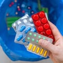 Persona se dispone a botar varios sellos de medicamentos en la basura.