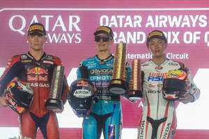 David Alonso (cent) exhibe el trofeo que ganó tras cruzar la meta primero en Lusail, durante la carrera de Moto3 en Catar. A la izquierda el japonés Taiyo Furusato . /Foto AP/Hussein Sayed)