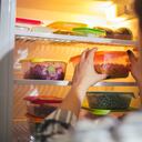 View at a fridge full of fresh raw food and a person choosing a container of veggies they're going to have for lunch.