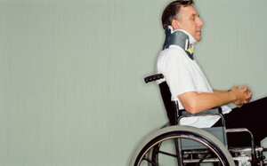 Man with neck brace in wheel chair in hospital.