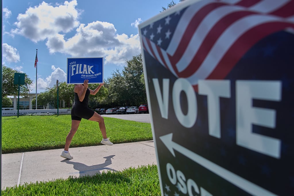 Yvette Allen, de Celebration, Florida, hace ejercicio mientras sostiene un cartel de la elección de la junta escolar local frente a la biblioteca West Osceola Branch, durante la votación anticipada para las elecciones primarias de Florida en Celebration, Florida, el jueves 13 de agosto de 2026.