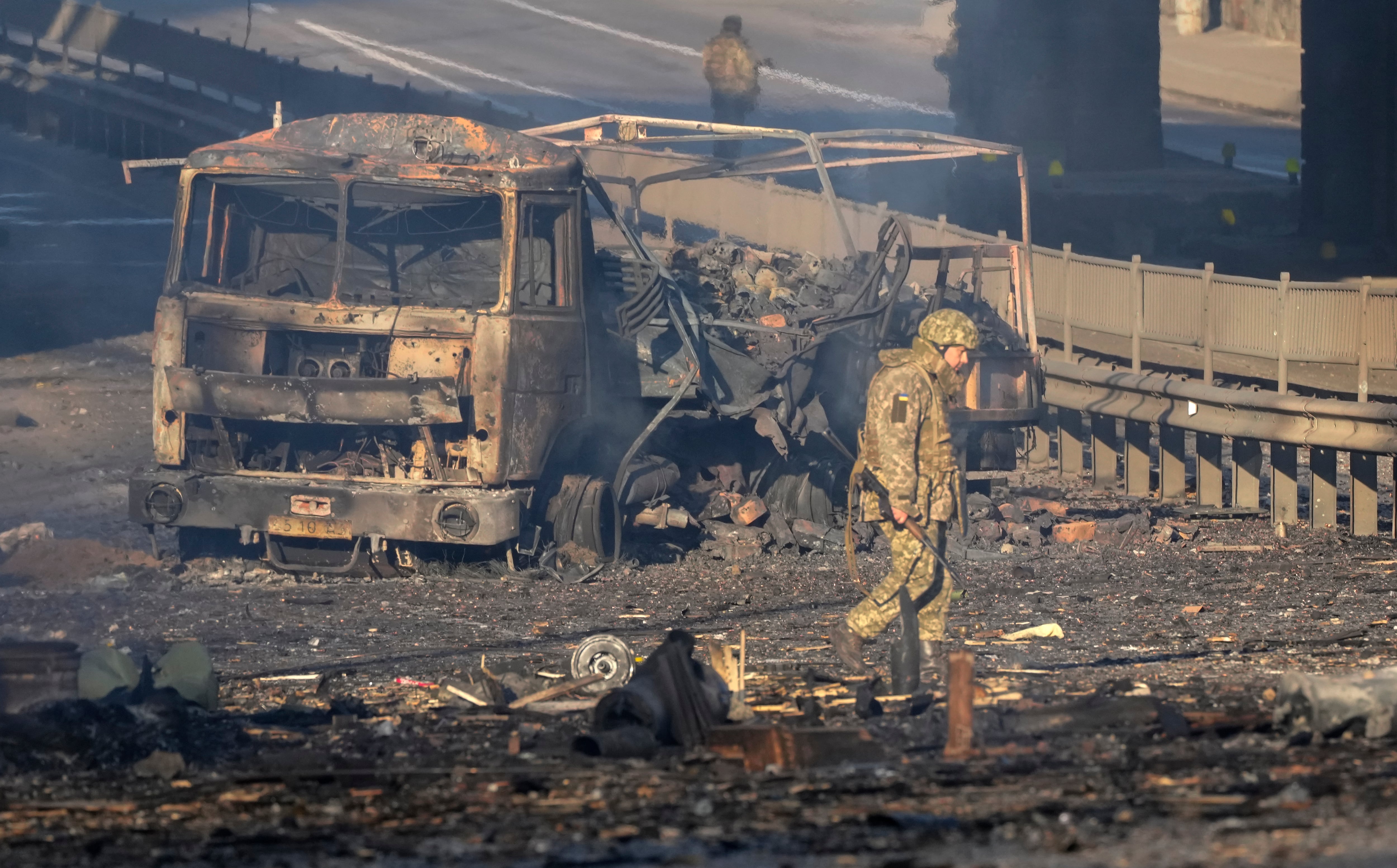 Un soldado ucraniano se desplaza entre los restos de un camión militar incendiado en una calle en Kiev, Ucrania, el sábado 26 de febrero de 2022. (AP Foto/Efrem Lukatsky)