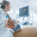 En el hospital, la toma de primer plano del médico realiza un procedimiento de ultrasonido/sonograma a una mujer embarazada. Transductor móvil obstétrico en el vientre de la futura madre.