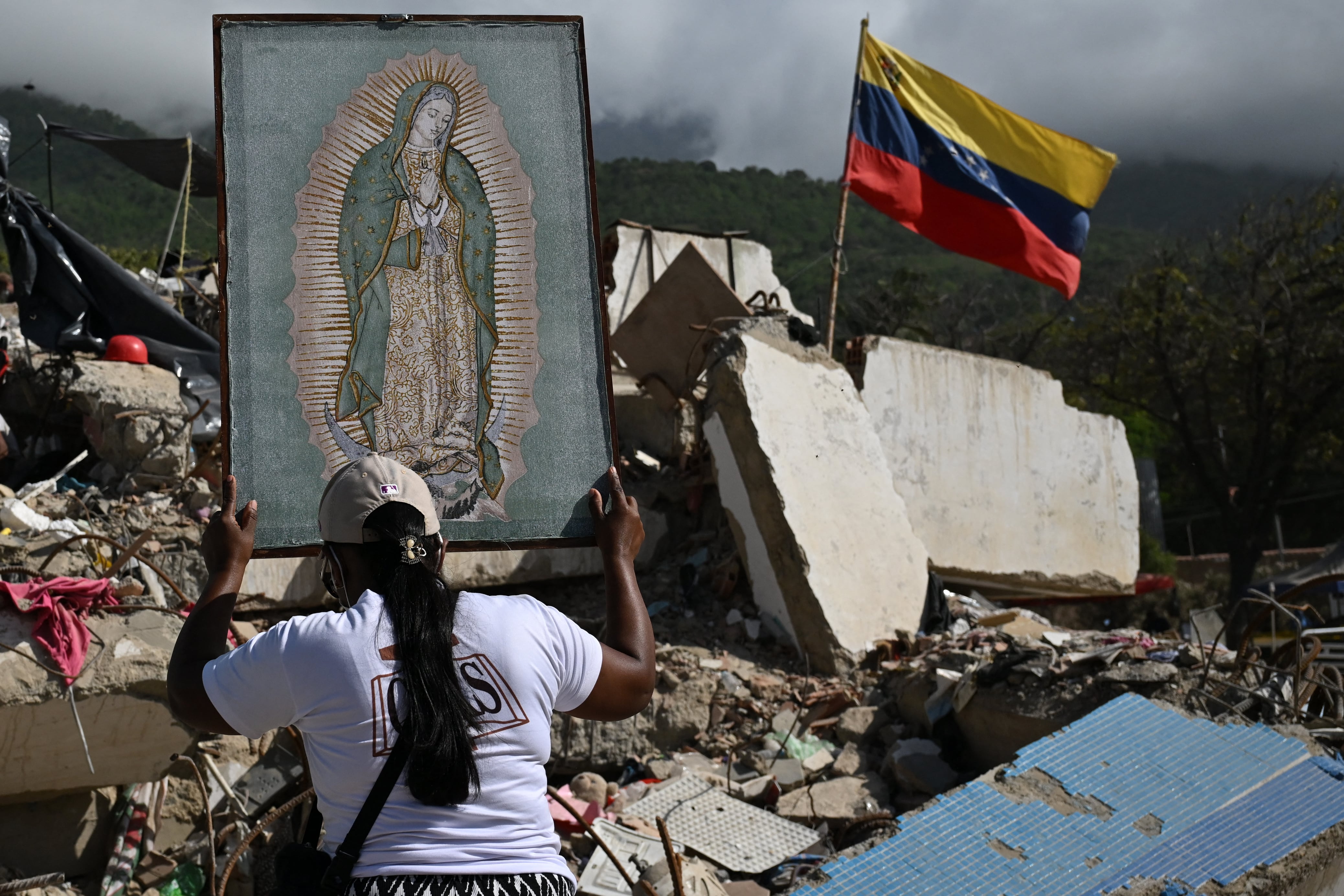 Una mujer sostiene una imagen de la Virgen de Guadalupe mientras voluntarios y familiares de las víctimas buscan los cuerpos de sus seres queridos entre los escombros de un edificio destruido por los terremotos del 24 de junio en Caraballeda, Venezuela, el 17 de julio de 2026.