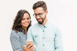 Mujer alegre feliz que muestra el mensaje en el teléfono a su novio. Mujer joven en casual y hombre con gafas en gafas posando aislado sobre fondo blanco. Concepto de buenas noticias