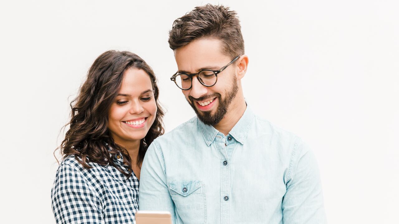 Mujer alegre feliz que muestra el mensaje en el teléfono a su novio. Mujer joven en casual y hombre con gafas en gafas posando aislado sobre fondo blanco. Concepto de buenas noticias