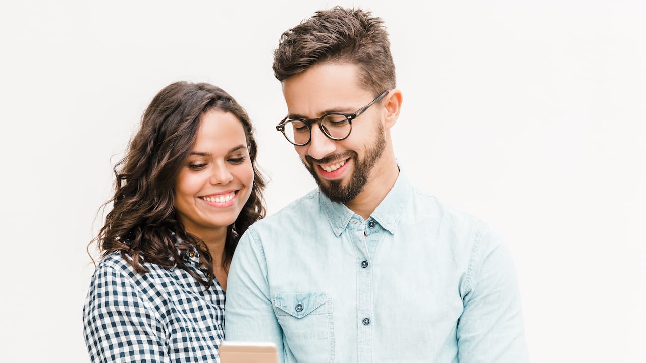 Mujer alegre feliz que muestra el mensaje en el teléfono a su novio. Mujer joven en casual y hombre con gafas en gafas posando aislado sobre fondo blanco. Concepto de buenas noticias
