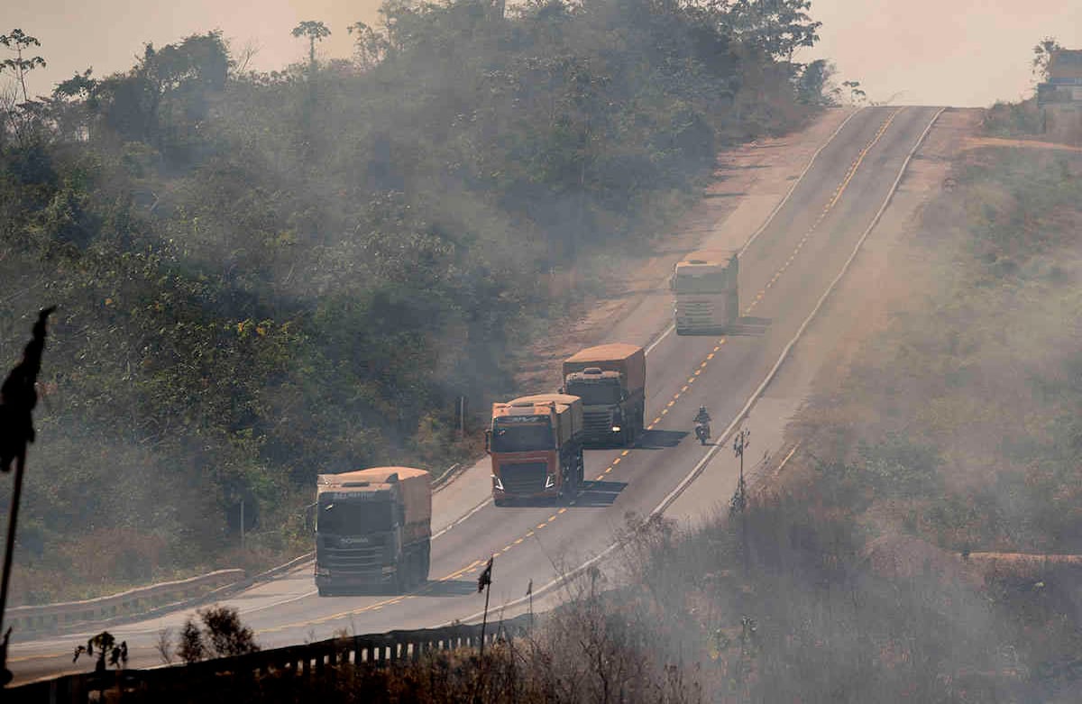 Camiones de carga viajan por la carretera BR-163 mientras el humo sale de un campo cercano consumido por el fuego, cerca de Novo Progresso, estado de Pará, Brasil, el sábado 15 de agosto de 2020. Según un agricultor local, los ganaderos iniciaron el incendio para limpiar la tierra para el cultivo de soja. Foto: Andre Penner / AP 